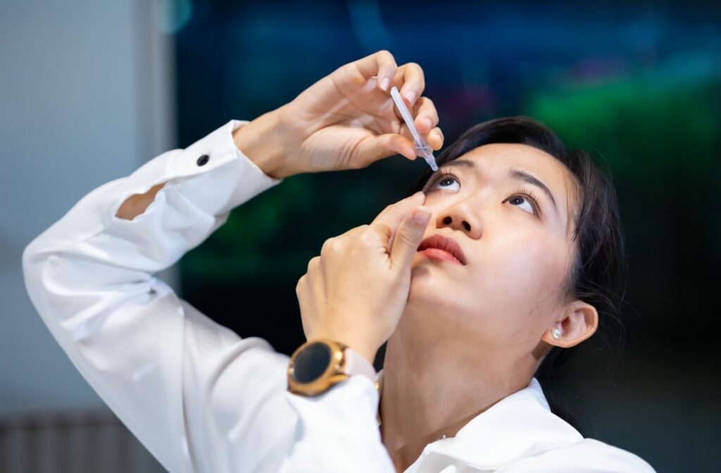 A business professional in a white button-up holds their eyelid open while applying eyedrops