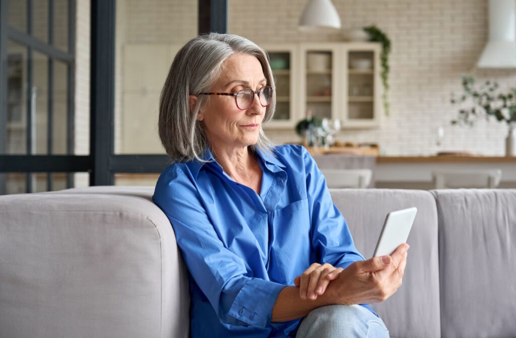 Older adult sitting comfortably on a couch reading a book while wearing reading glasses.