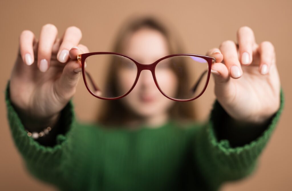 Close-up of reading glasses being held up, showing clear focus through the lenses with a blurred background around them.