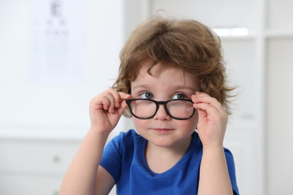 A child looking over the top of a pair of glasses they are wearing for their myopia