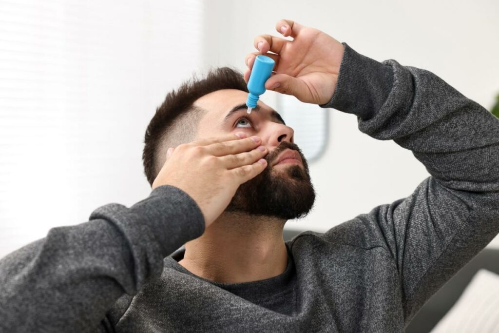 A person looking up while they place eye drops in their eye