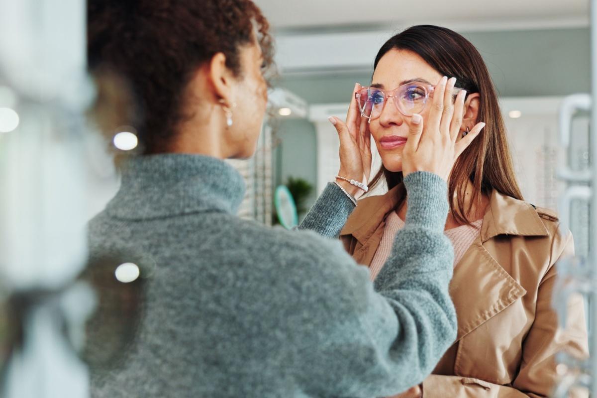 An optician helping a patient try on a new pair of pink framed glasses