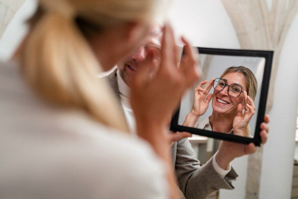 Person trying on a pair of glasses and looking into a small mirror