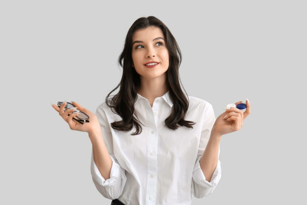 a person holding glasses in one hand and contact lens in the other